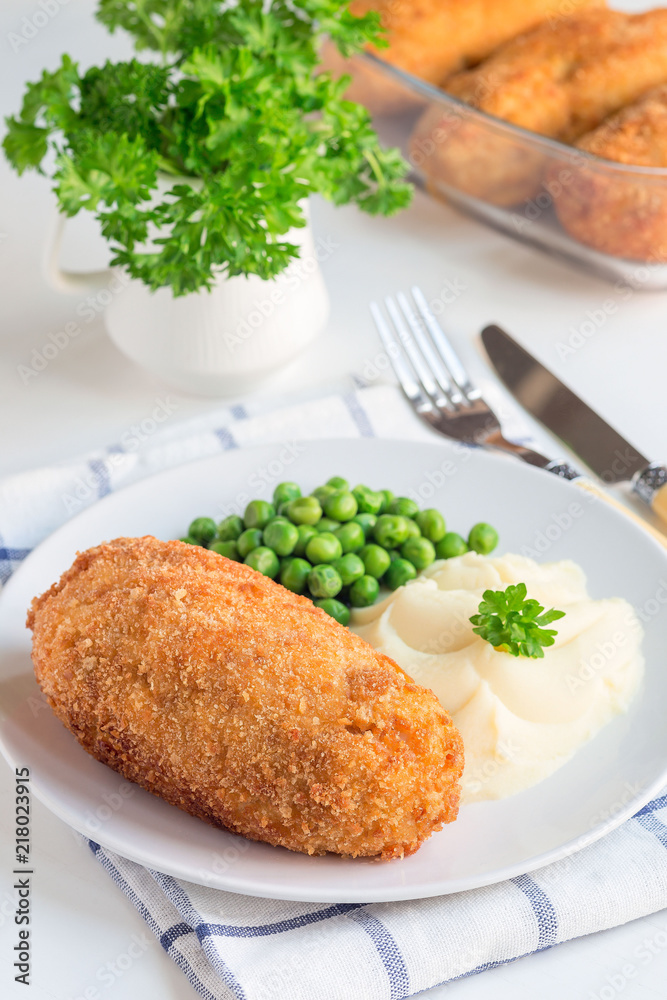 Chicken Kiev, ukrainian cuisine. Chicken cutlets in breadcrumbs stuffed with butter and herbs, served with mashed potato and green peas, vertical