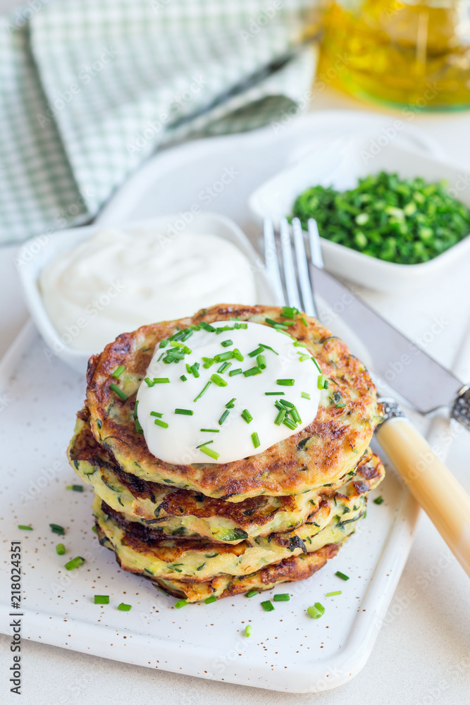 Vegetarian zucchini fritters or pancakes, served with greek yogurt and green onion on ceramic plate, vertical Vegetarian zucchini fritters or pancakes, served with greek yogurt and green onion on ceramic plate, vertical
