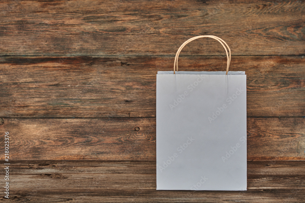 Mock-up of white craft paper package with handles, empty shopping bag with area for your logo or design, wooden board in the background, food delivery, sale, consumerism and advertising concept. Mock-up of white craft paper package with handles, empty shopping bag with area for your logo or design, wooden board in the background, food delivery, sale, consumerism and advertising concept.