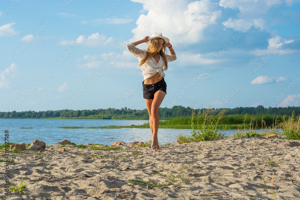 Beautiful happy young woman in a hat and in shorts running along the seashore