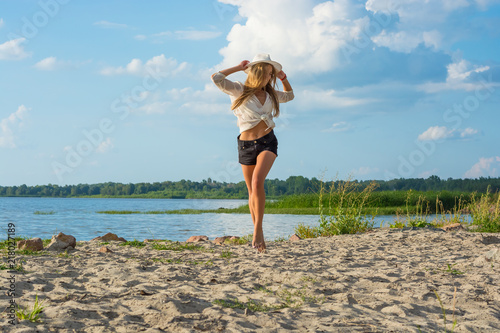 Obraz na płótnie Beautiful happy young woman in a hat and in shorts running along the seashore w salonie
