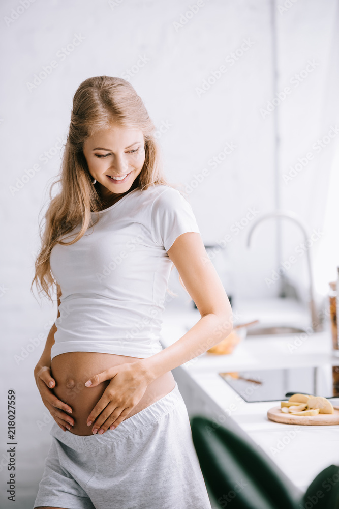 smiling beautiful pregnant woman with hands on belly standing in kitchen at home smiling beautiful pregnant woman with hands on belly standing in kitchen at home