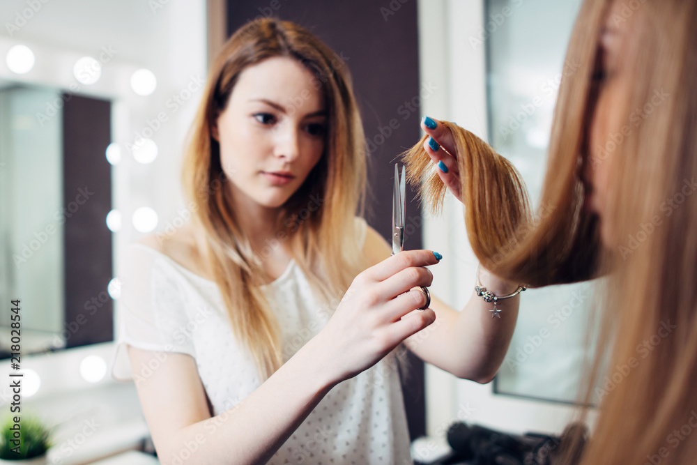 Φωτογραφία Young pretty hairdresser wearing casual clothes holding strand of long hair betw