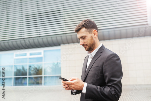 A handsome businessman using a smartphone. working by using smart phone in remote working concept. Business and information technology concept. standing street with city in the background