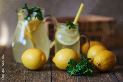 Homemade lemonade with mint and ice in jug, with fresh lemons over wooden background. Delicious and juicy lemonade, full of useful vitamins and antioxidants. Healthy and detox summer drink.