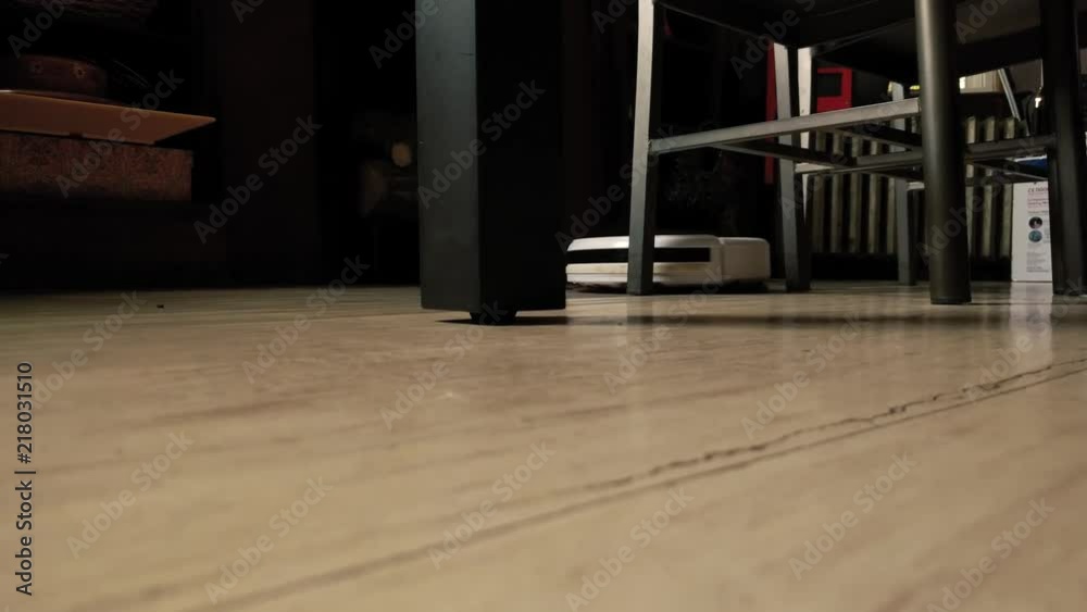 Robotic Vacuum Cleaner sweeping floor around table and chairs. Floor level view. Robotic Vacuum Cleaner sweeping floor around table and chairs. Floor level view.