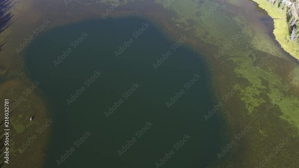 Aerial view above lake moving down towards the water with person kayaking on the surface. Aerial view above lake moving down towards the water with person kayaking on the surface.