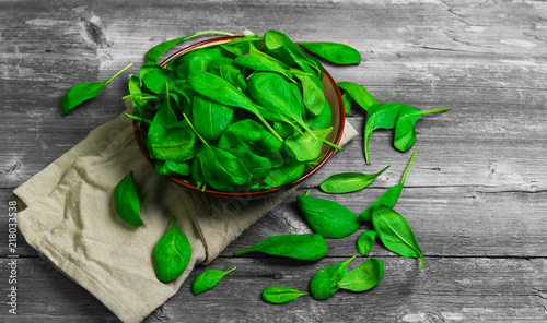 Fresh green leaves mini spinach in ceramic bowl. Spinach leaves on the gray wooden rustic background.