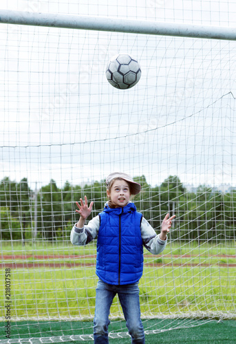 Little girl stands in the football gate as a goalkeeper and wants to catch the ball in her hands