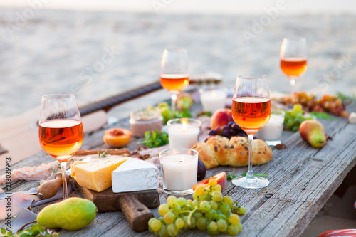 Picnic on beach at sunset in boho style. Romantic dinner, friends party, summertime, food and drink concept