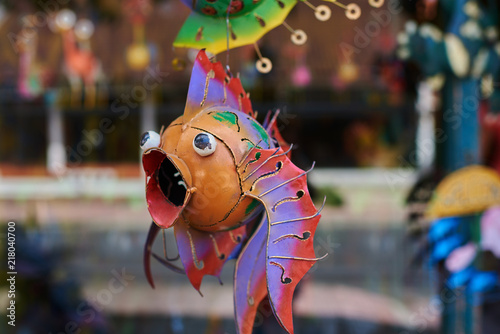 Colorful souvenir background. Hanging decoration in the market. Handmade metallic fish hanging on the tourist market. Sale of souvenirs. Funny handmade fishes with bright colorful patterned.