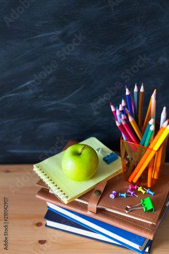 Back to School cocept. Still life with school books, pencils and apple against blackboard background