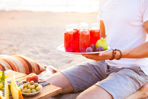 Happy man holds a dish with a drinks red juice at sunset. Picnic theme on the beach photo