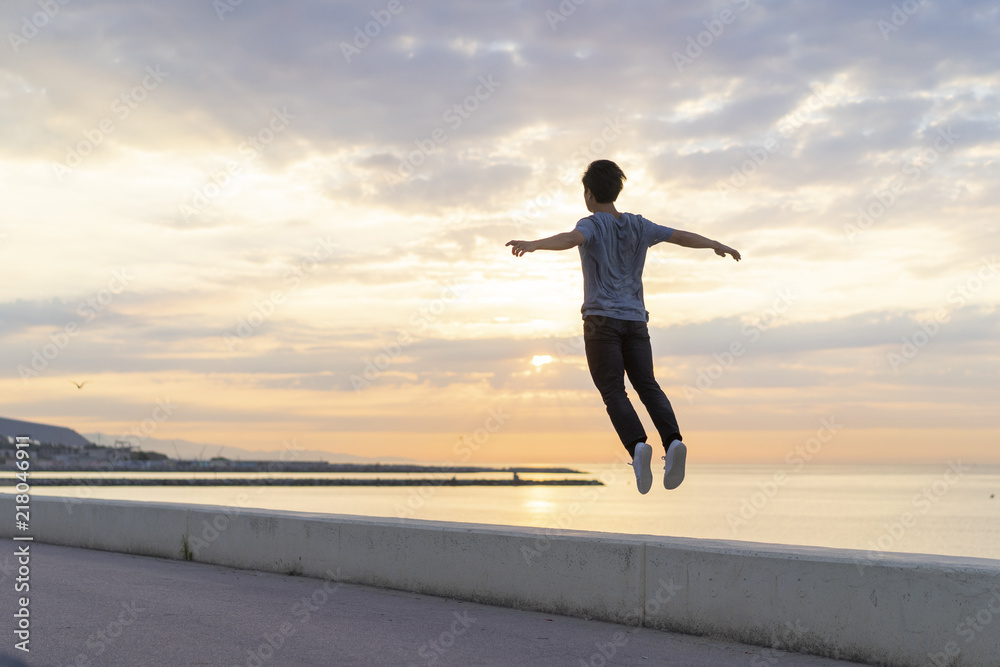 Young Chinese man jumping on wall at the beach Young Chinese man jumping on wall at the beach
