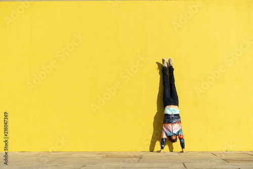 Acrobat doing handstand in front of a yellow wall photo