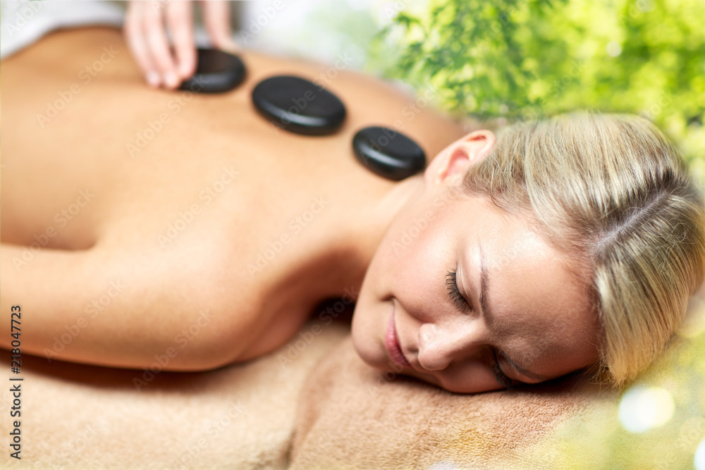 Obraz premium beauty, wellness and relaxation concept - close up of beautiful young woman having hot stone massage in spa over green natural background
