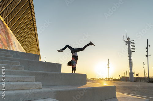 Acrobat doing handstand on stairs at sunrise