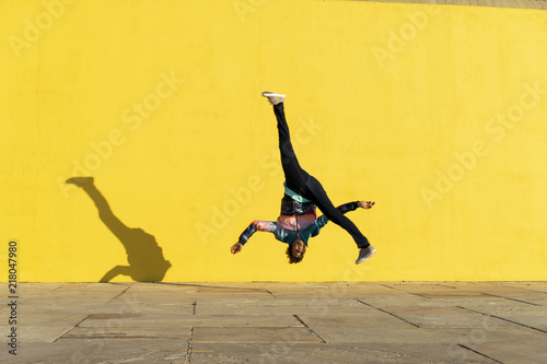 Acrobat jumping somersaults in front of yellow wall photo
