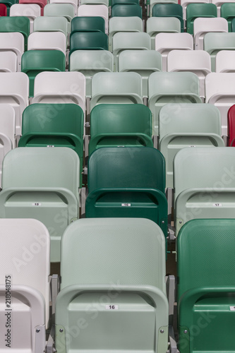 Rows of empty chairs on tribunes of a modern stadium without spectators and colored chairs with numbers in the center of the arena