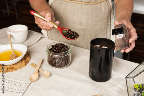 Women's hands putting some coffee beans by wooden spoon in black coffee-grinder