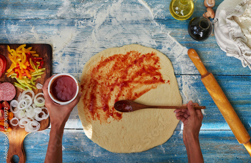 Obraz na płótnie Chef hand is spreading pasteurized tomato paste into a Pizza base
