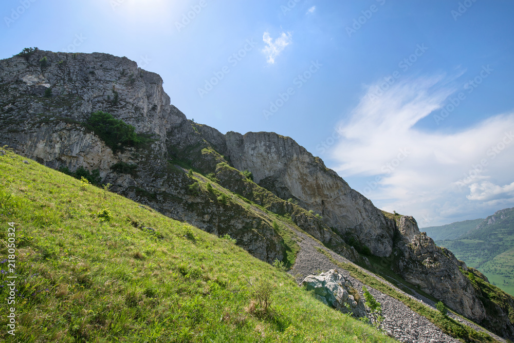 Sunny summer day, white clouds over mountain peak, where tourists climb to conquer fear, find courage and develop lateral thinking skills to overcome the difficulty of climbing a mountain. Small road