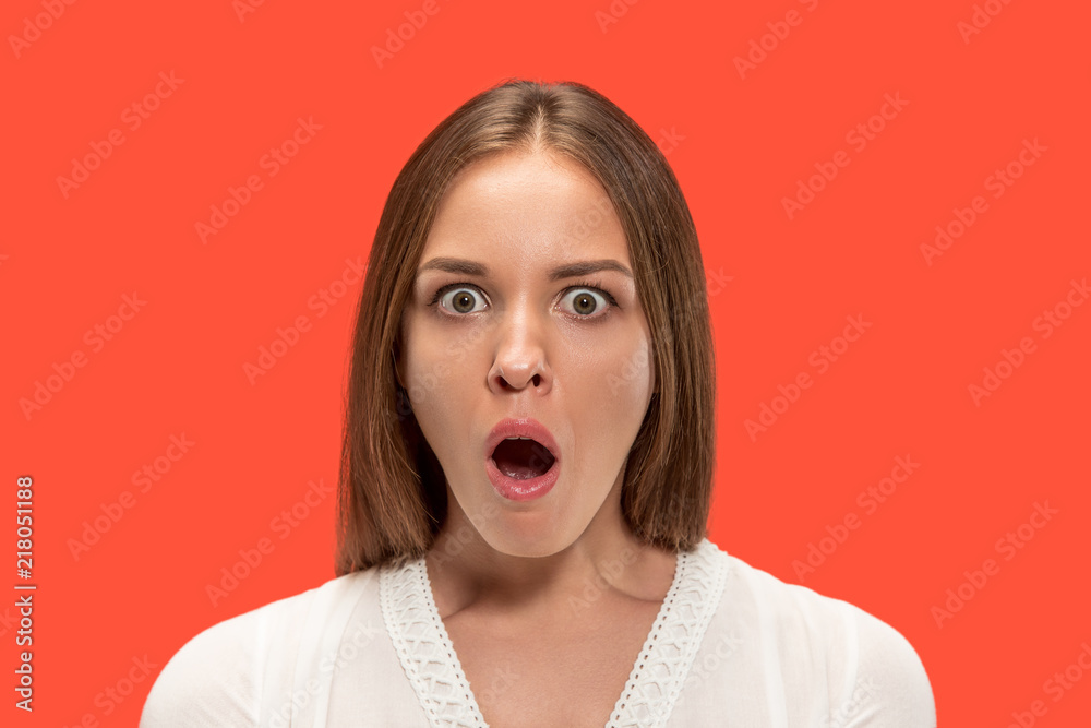 Wow. Beautiful female half-length front portrait isolated on red studio backgroud. Young emotional surprised woman standing with open mouth. Human emotions, facial expression concept.