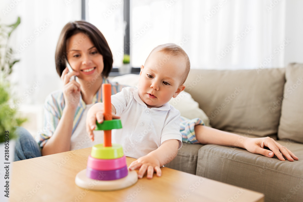 family, child and motherhood concept - happy baby boy playing developmental toy and mother calling on smartphone at home family, child and motherhood concept - happy baby boy playing developmental toy and mother calling on smartphone at home