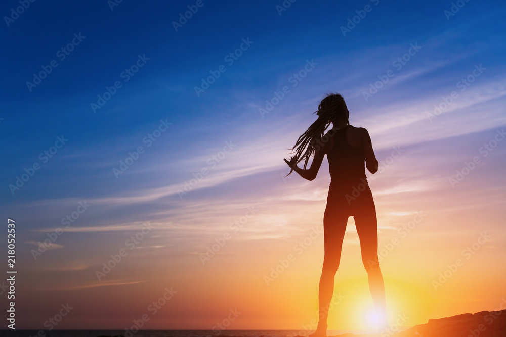 Silhouette of young slim woman on the sea coast during amazing sunset.