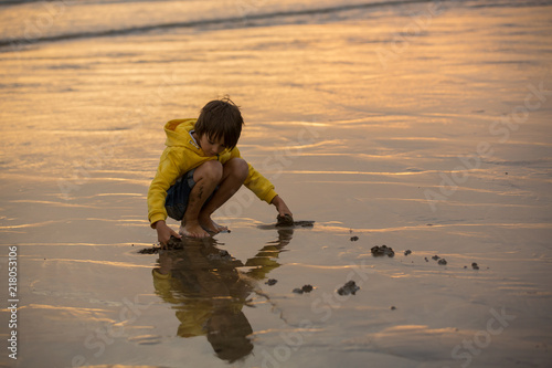 Cute beautiful child, boy playing on the beach with sand and running in the water on sunset