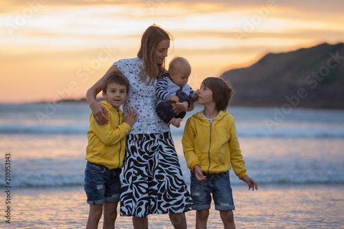 Young mother with her beautiful children, enjoying the sunset over the ocean on a low tide in Devon