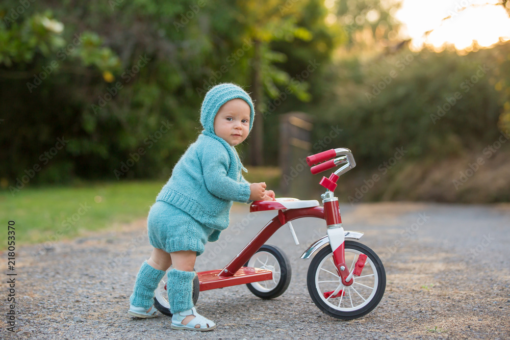 Cute toddler child, boy, playing with tricycle in backyard on sunset Cute toddler child, boy, playing with tricycle in backyard on sunset