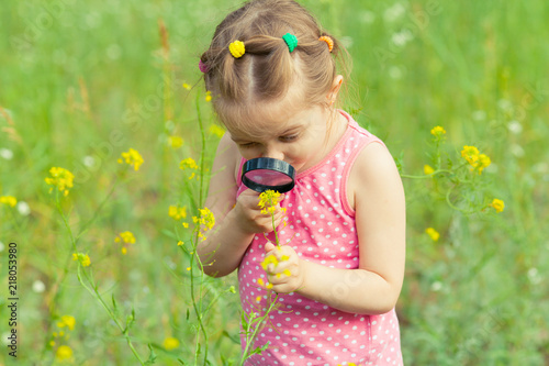 Canvas-taulu Young girl exploring nature in the meadow with a magnifying glass looking at flowers