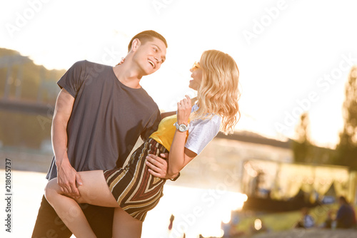 young smiling couple hugging on river beach in evening and looking at each other