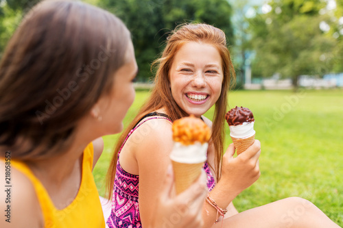 leisure and friendship concept - happy smiling teenage girls or friends eating ice cream at picnic in summer park