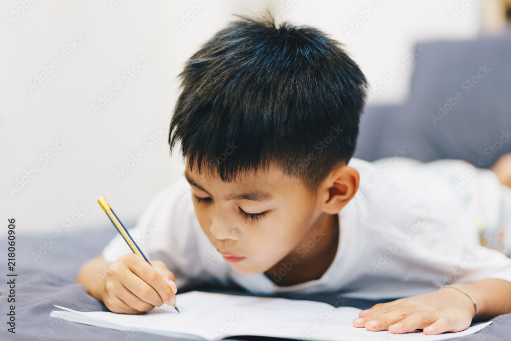 Little Asian boy doing homework by use pencil writing on notebook for writing book at night Little Asian boy doing homework by use pencil writing on notebook for writing book at night