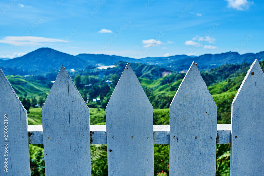 Wooden fence  with green grass and mountain peaks in background.