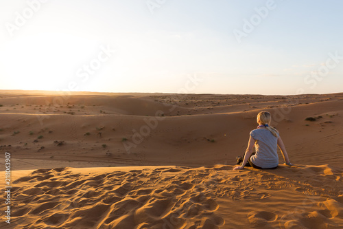 Blonde girl relaxes at sunset in Wahiba sands, Oman