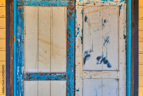 Weathered, wooden door in an old house. Old wooden door with leaving paint. Part old house yellow wall with blue and white door. Weathered painted wooden surface. Vintage color.Grunge wood texture.