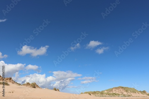 Little fluffy white clouds in blue sky over sand dunes
