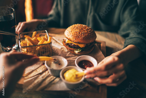 Group of friends eating at fast food. Friends are eating burgers while spending time together in cafe.Tasty grilled beef burger with lettuce and mayonnaise served on pieces of brown paper. photo