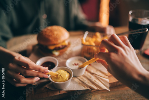 Group of friends eating at fast food. Friends are eating burgers while spending time together in cafe.Tasty grilled beef burger with lettuce and mayonnaise served on pieces of brown paper.