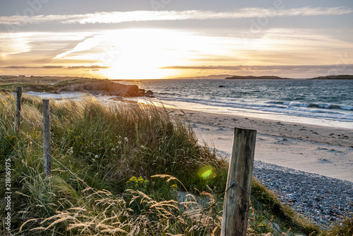 Pretty sunset beach behind a wooden fence and long grass. Taken in Renvyle  Ireland.