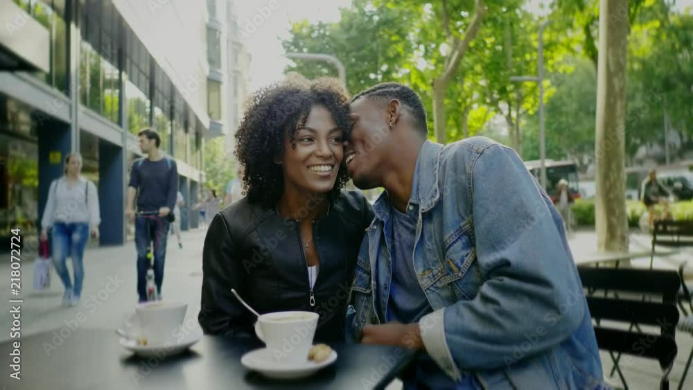 Young happy black couple drinking coffee in street cafe