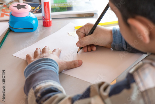 Creative workshop for kids. Little boy drawing on white paper at school. Glue, colorful pencils and star shaped paper cutter on table. Making decorations. Concept of art, crafts and kids having fun