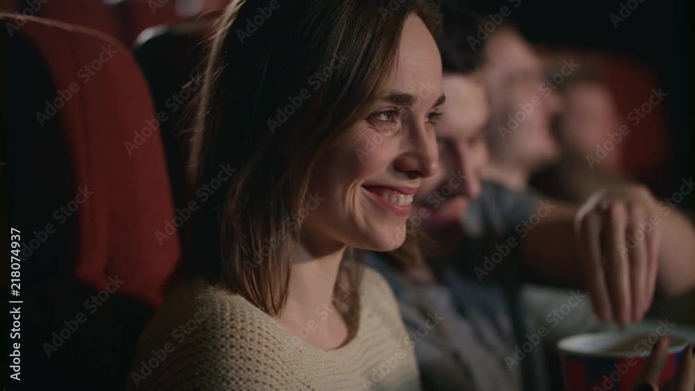 Smiling woman watching movie. Close up of beautiful girl laughing in cinema in slow motion. Boyfriend and girlfriend have fun at movie theater. Romantic date at cinema. Love couple watch comedy film