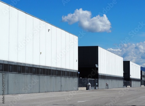 A row of large black and white industrial warehouse buildings with the road in front .