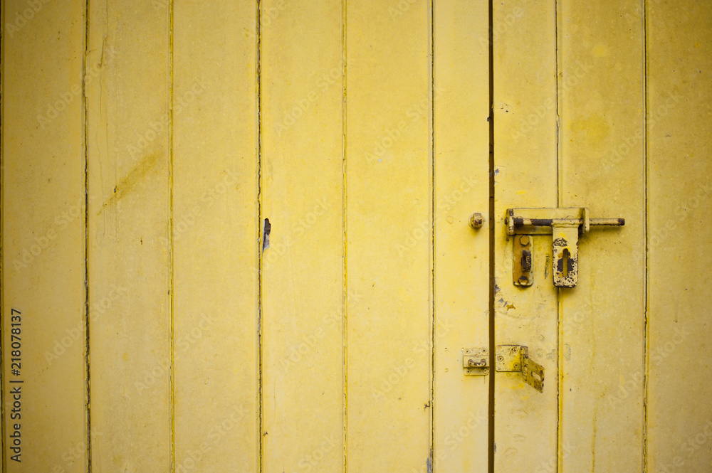 Close-up view of a weathered yellow color door with an open rusty latch