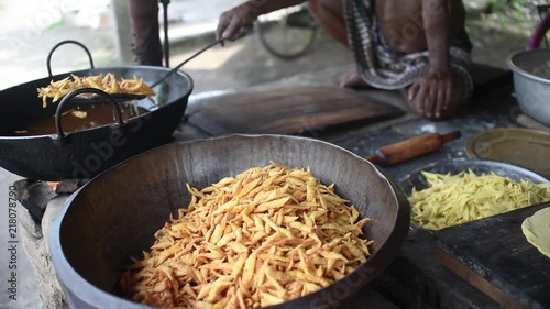 A man picking the frying Indian street snacks Nimki from a Wok with mesh skimmer and putting them in a big utensil photo