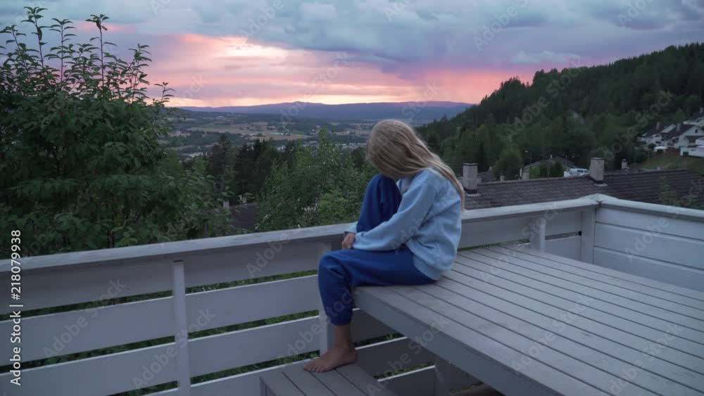 Girl sitting on a table, feeling sad. Evening sky in the background Girl sitting on a table, feeling sad. Evening sky in the background